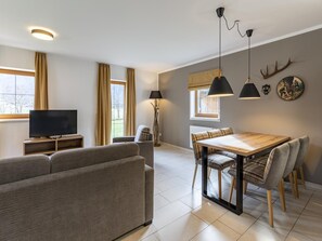Ein modernes Wohnzimmer mit Sofa, Fernseher, Esstisch und Stühlen.