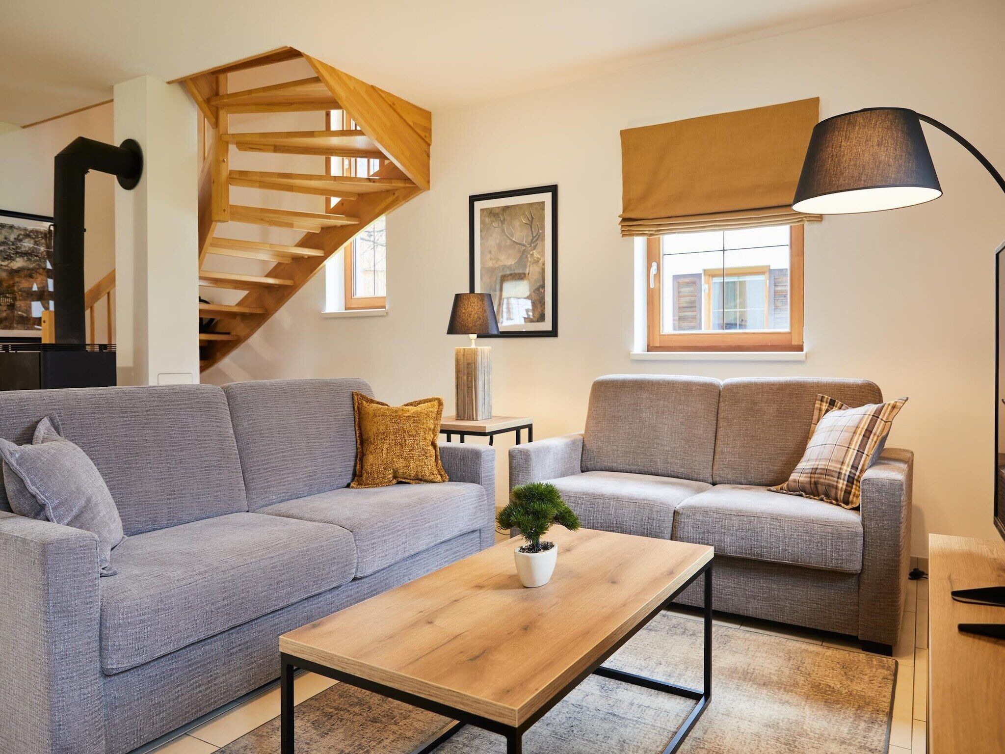 Ein modernes Wohnzimmer mit einer Holztreppe, zwei Sofas, einem Couchtisch und einer Lampe.