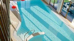 Una piscina interna con acqua cristallina, un trampolino e vista sull'esterno attraverso ampie finestre.