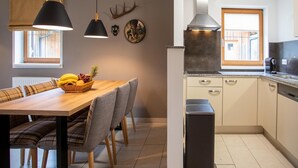 Una cucina moderna con un tavolo da pranzo in legno, sedie, lampade a sospensione e una cappa aspirante in acciaio inossidabile.