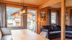 Een houten interieur met een eettafel, bank en uitzicht op een berglandschap door grote ramen.