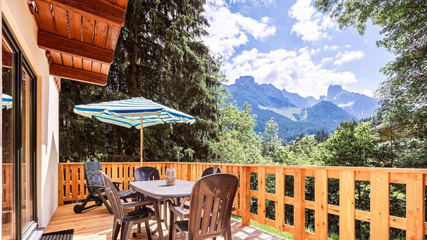 Een houten terras met een tafel, stoelen en een parasol, met uitzicht op bergen.