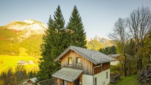 Een houten hut met een balkon, omgeven door bos en bergen.