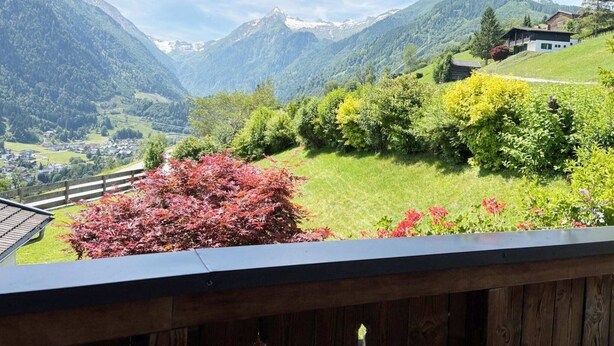 Un balcon offrant une vue sur un paysage montagneux, comprenant un village et une maison située sur une colline.