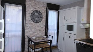 A kitchen with a stone wall, a clock, a dining table with chairs, and white cabinets.