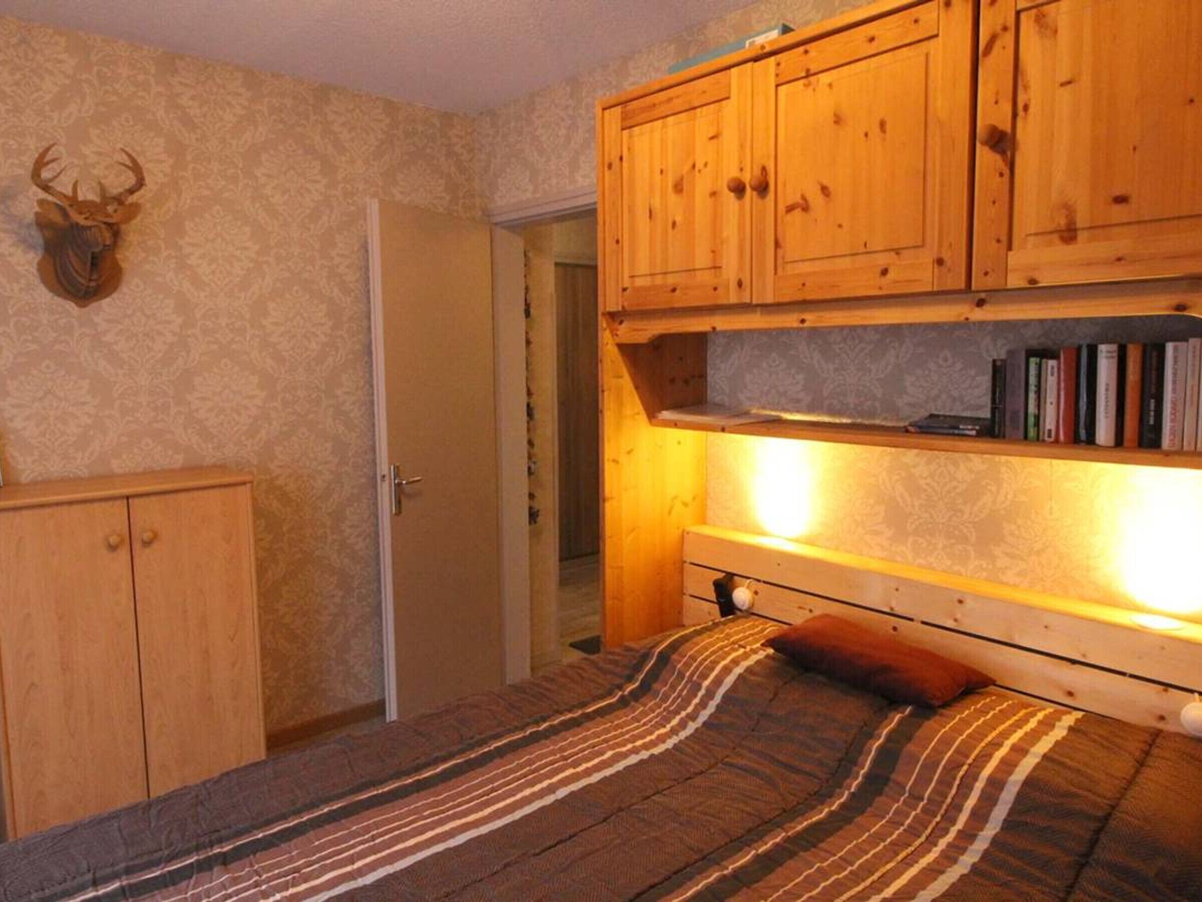 Un dormitorio con cama, armarios de madera, cabeza de ciervo montada y una estantería.