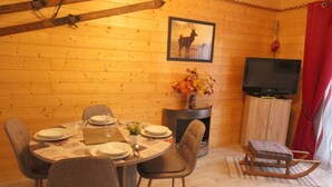A cozy wooden room with a dining table set for four, a fireplace, a television, and a sled.