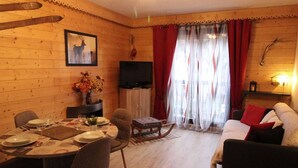 A cozy log cabin interior with a dining area, a sofa, and a TV.