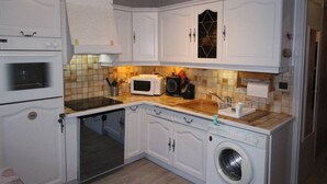 A compact kitchen with white cabinetry, a microwave, a built-in oven, a washing machine, and a tiled backsplash.