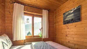 En stuga med träpanel, ett rum med en säng, ett fönster med gardiner, en vas med blommor och en tavla på väggen.
