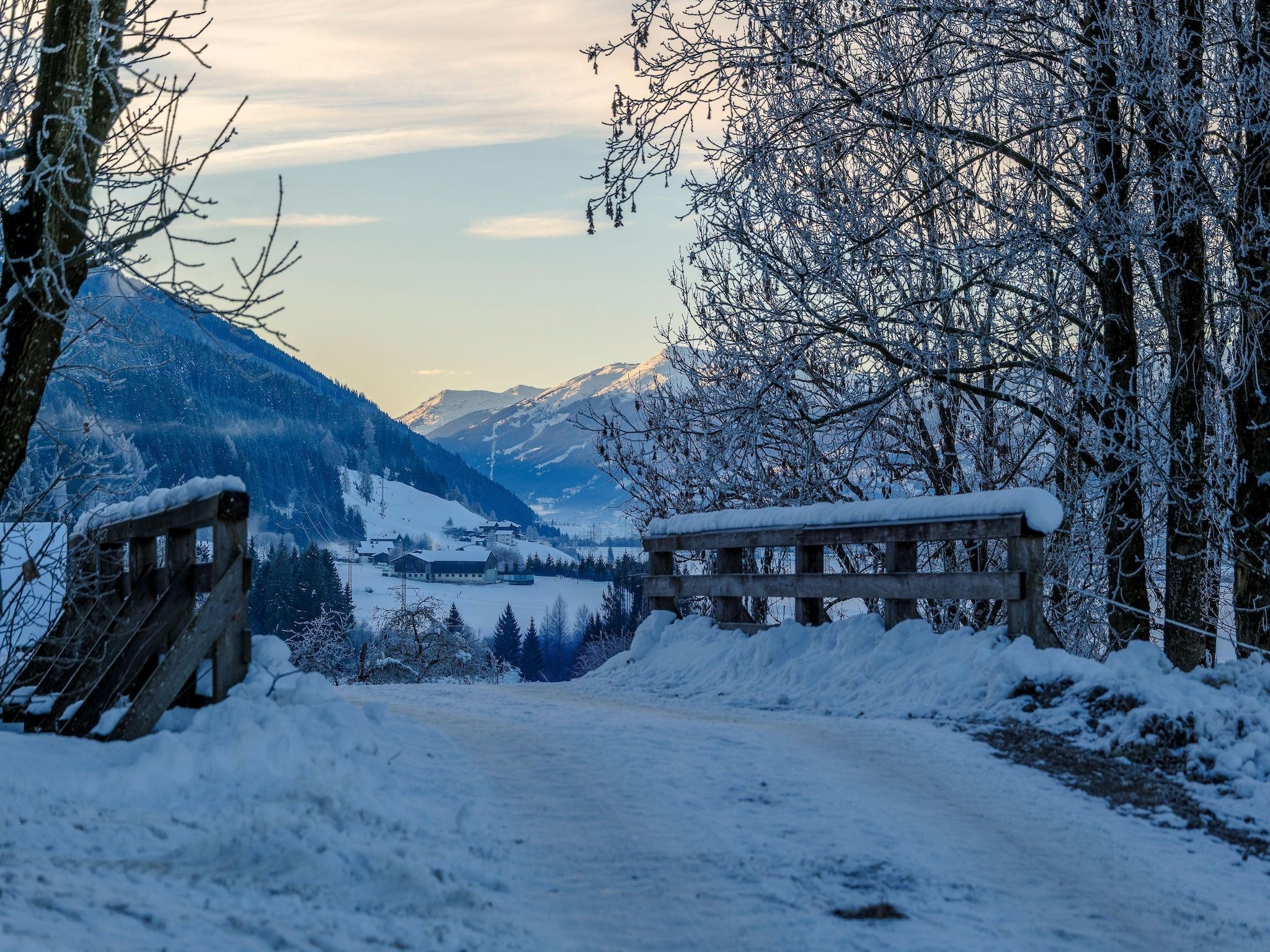 A snow-covered landscape with a wooden bench and a wooden fence.