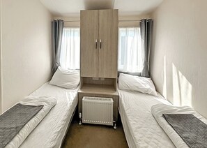 Alojamiento pequeño de una sola habitación con dos camas individuales, armario empotrado y radiador.