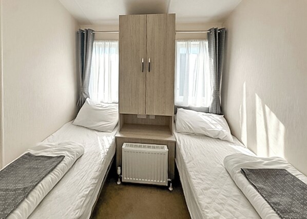 A small, single-room accommodation with two single beds, a built-in wardrobe, and a radiator.