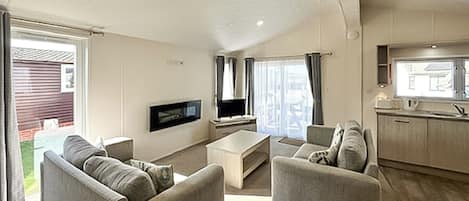 A living room with a flat-screen TV, two sofas, a coffee table, and a sliding glass door leading to a patio.