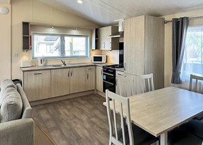A compact kitchen with a dining table, chairs, a microwave, and a stove. - Superior Lodge (sleeps 8) (Bacton-on-Sea)