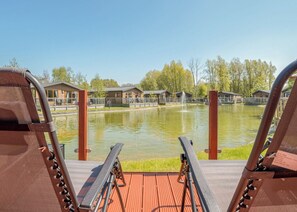 A deck with a view of a pond, wooden buildings, and a clear sky.