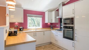 A modern kitchen with white cabinets, a wooden countertop, a built-in oven, and a window with a view of trees.