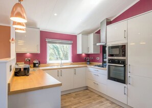 A modern kitchen with white cabinets, a wooden countertop, a built-in oven, and a window with a view of trees. - 3 bedroom accommodation in Carnforth (Carnforth)