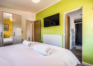 A hotel room with a bed, a television mounted on the wall, and a wooden door leading to a shower area.