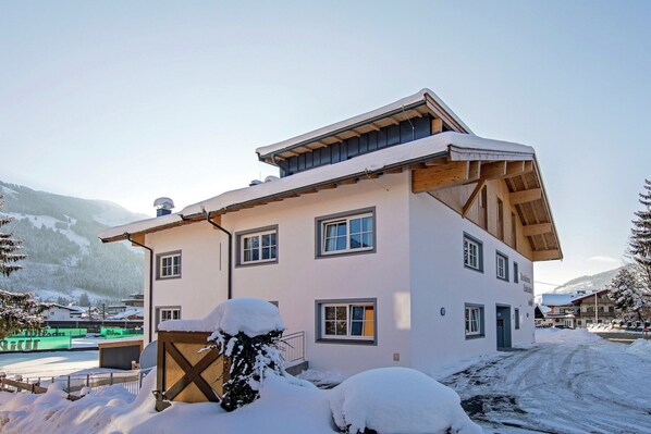 Un edificio de dos pisos con techo inclinado, múltiples ventanas y un entorno cubierto de nieve.