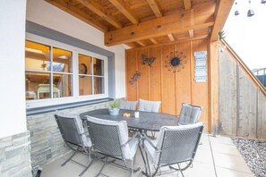 Un patio al aire libre con una mesa redonda y seis sillas, vigas de madera en el techo y una pared de madera con detalles decorativos.