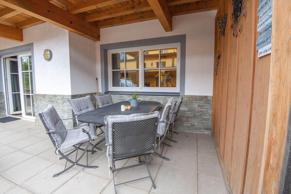 An outdoor patio with a round table and chairs, a stone wall, and a wooden ceiling. - Modern Apartment in Brixen im Thale near Ski Area (Brixen im Thale)