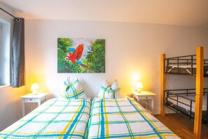 Habitación de hotel con una cama, dos mesitas de noche, una lámpara, una cama nido y un cuadro de un loro.