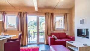 A modern room with a red sofa, a red armchair, a wooden desk, and a television. - Cosy chalet with infrared sauna (Murau)
