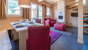 A wooden interior with a dining area, red chairs, a fireplace, and a TV. - Cosy chalet with infrared sauna (Murau)