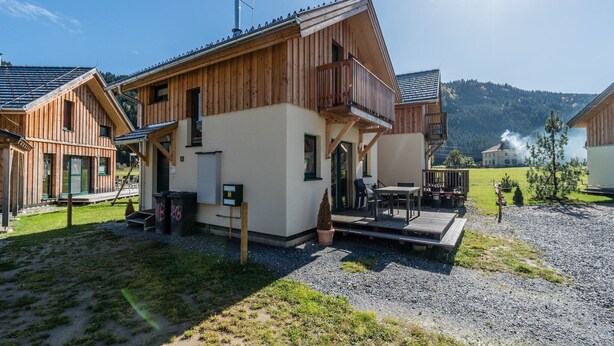 A wooden chalet with a balcony, a small outdoor seating area, and a view of the surrounding landscape. - Cosy chalet with infrared sauna (Murau)