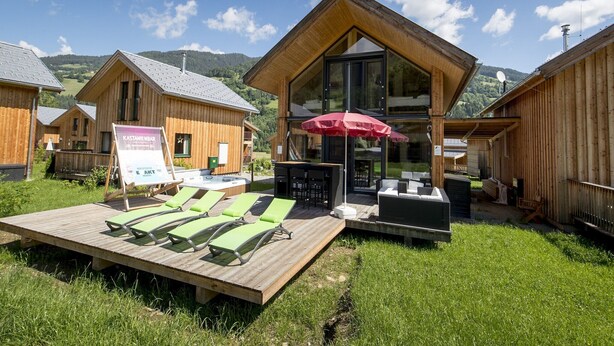 A wooden cabin with a deck, lounge chairs, and a glass-enclosed patio area. - Comforting chalet with whirlpool (Sankt Georgen am Kresichberg)