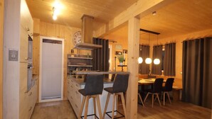 A wooden interior with a kitchen, dining area, and bar stools. - Comforting chalet with whirlpool (Sankt Georgen am Kresichberg)