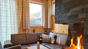 A cozy living room with a fireplace, a sofa, a coffee table, and curtains with a deer pattern. - Comforting chalet with whirlpool (Sankt Georgen am Kresichberg)