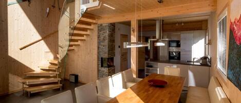 Un intérieur moderne avec un escalier en bois, un coin repas doté d’une longue table et une cuisine ouverte sur le reste de l’espace.