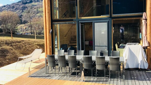 A modern building with large glass windows, a deck with outdoor seating, and a view of a hilly landscape. - Chalet in Sankt Georgen on Ski Slopes (Kreischberg Murau)