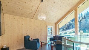 A modern living room with wooden walls, a glass table, and a view of a forest. - Chalet in Sankt Georgen on Ski Slopes (Kreischberg Murau)