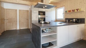 A modern kitchen with wooden walls, a central island, and built-in appliances. - Chalet in Sankt Georgen on Ski Slopes (Kreischberg Murau)