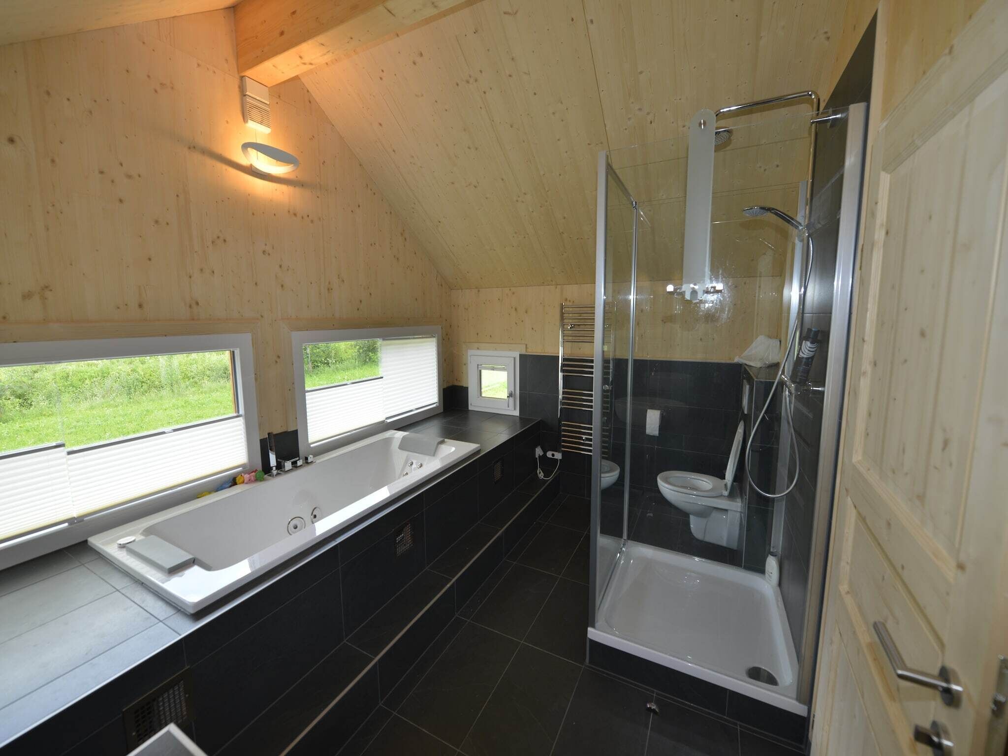 A modern bathroom with a large bathtub, a separate shower area, and a window providing a view of greenery.