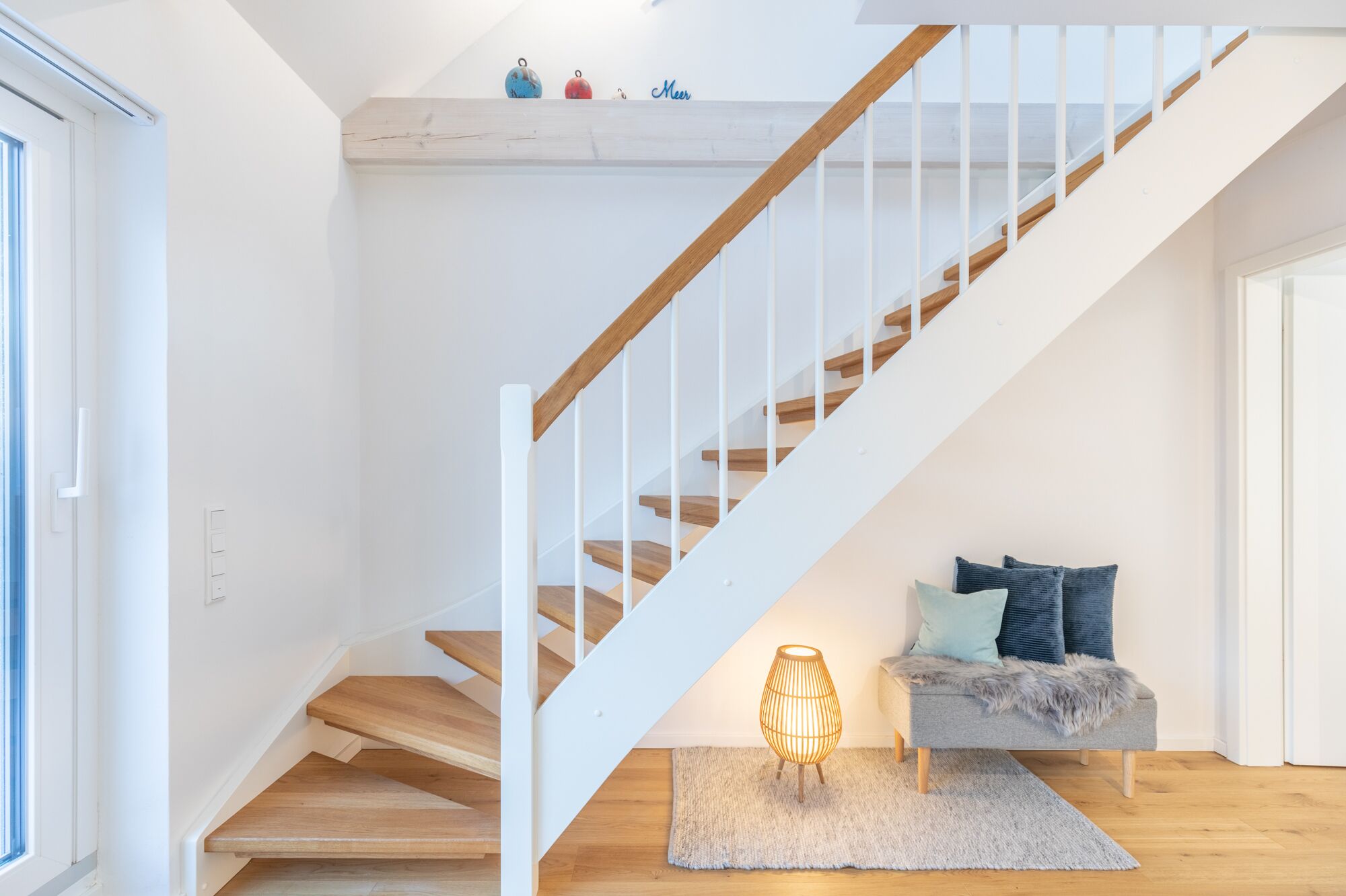 Una escalera con escalones de madera y barandillas blancas, que conduce a una plataforma con un banco y una lámpara.