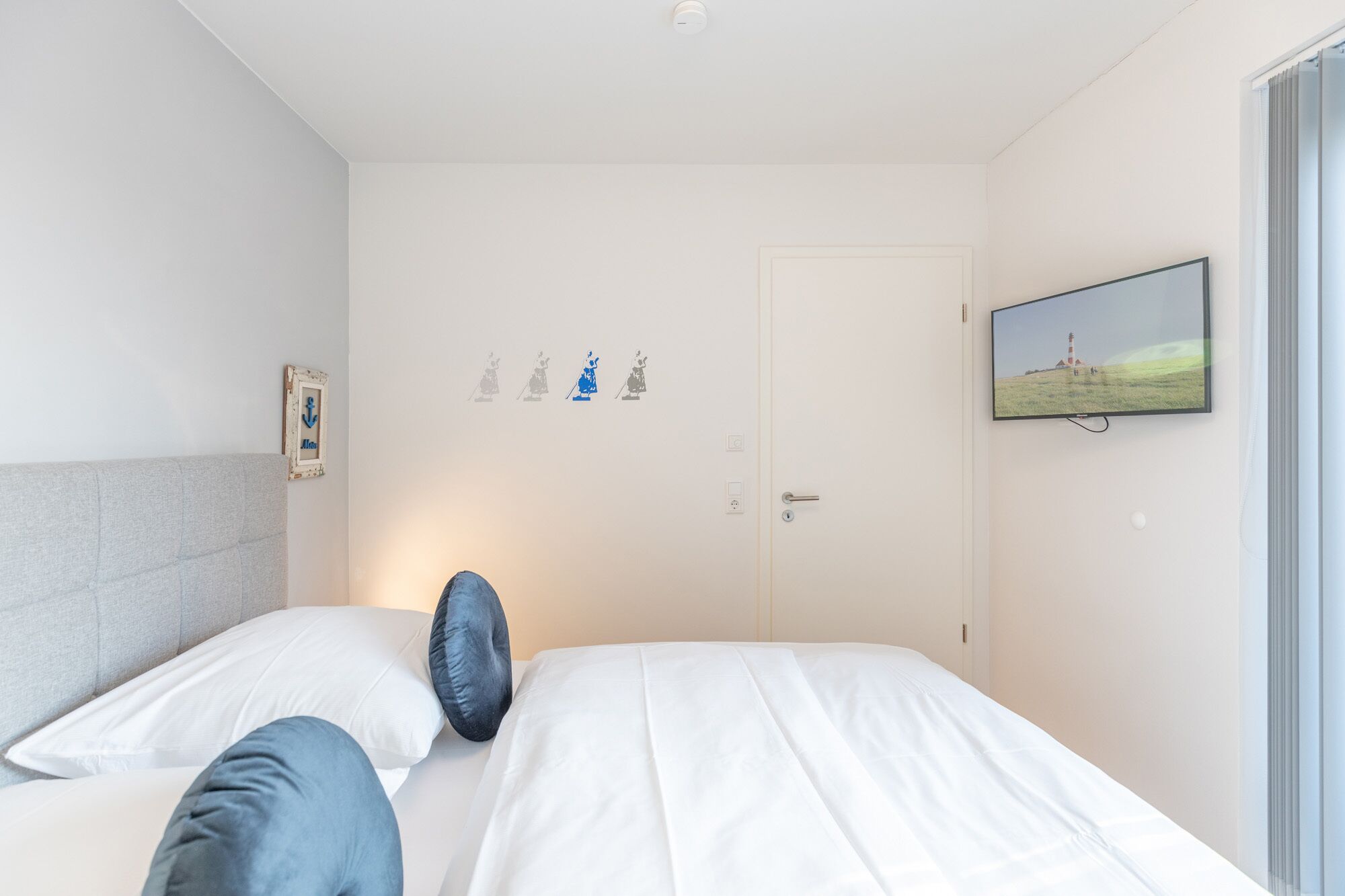 Un dormitorio con cama, almohadas, televisión en la pared y una puerta con imagen de un faro.
