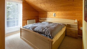 A bedroom with a wooden ceiling, a bed with a headboard, a bedside table, and a window with a view of trees. - Chalet in Turracher Höhe near Ski Slopes (Turracher Höhe)