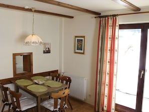 Un comedor con una mesa de madera, sillas, una lámpara colgante y una ventana con cortinas.