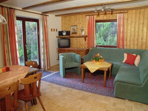 Relax in this inviting living room with a sofa, dining table, and TV, surrounded by large windows and lush views.