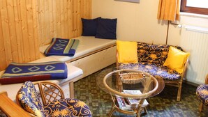 Una habitación acogedora con pared de madera, un sofá con cojines estampados, una mesita con una cesta y una ventana con cortinas.