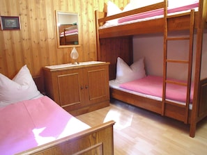 Habitación con literas, un armario de madera, una mesita de noche y un espejo en la pared.