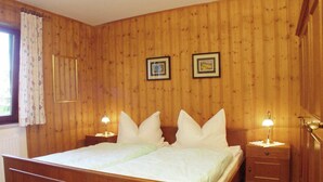 Un dormitorio con paneles de madera, una cama, dos mesitas de noche y dos cuadros enmarcados en la pared.