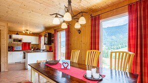 Un intérieur en bois comprenant une table à manger, des chaises, un coin cuisine et une vue sur l’extérieur.
