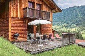 Una cabaña de madera con terraza, mobiliario exterior y una parrilla.