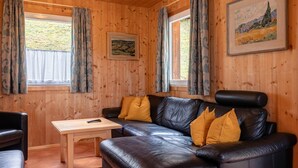Un intérieur en bois avec un canapé en cuir, une petite table et deux fenêtres avec des rideaux.