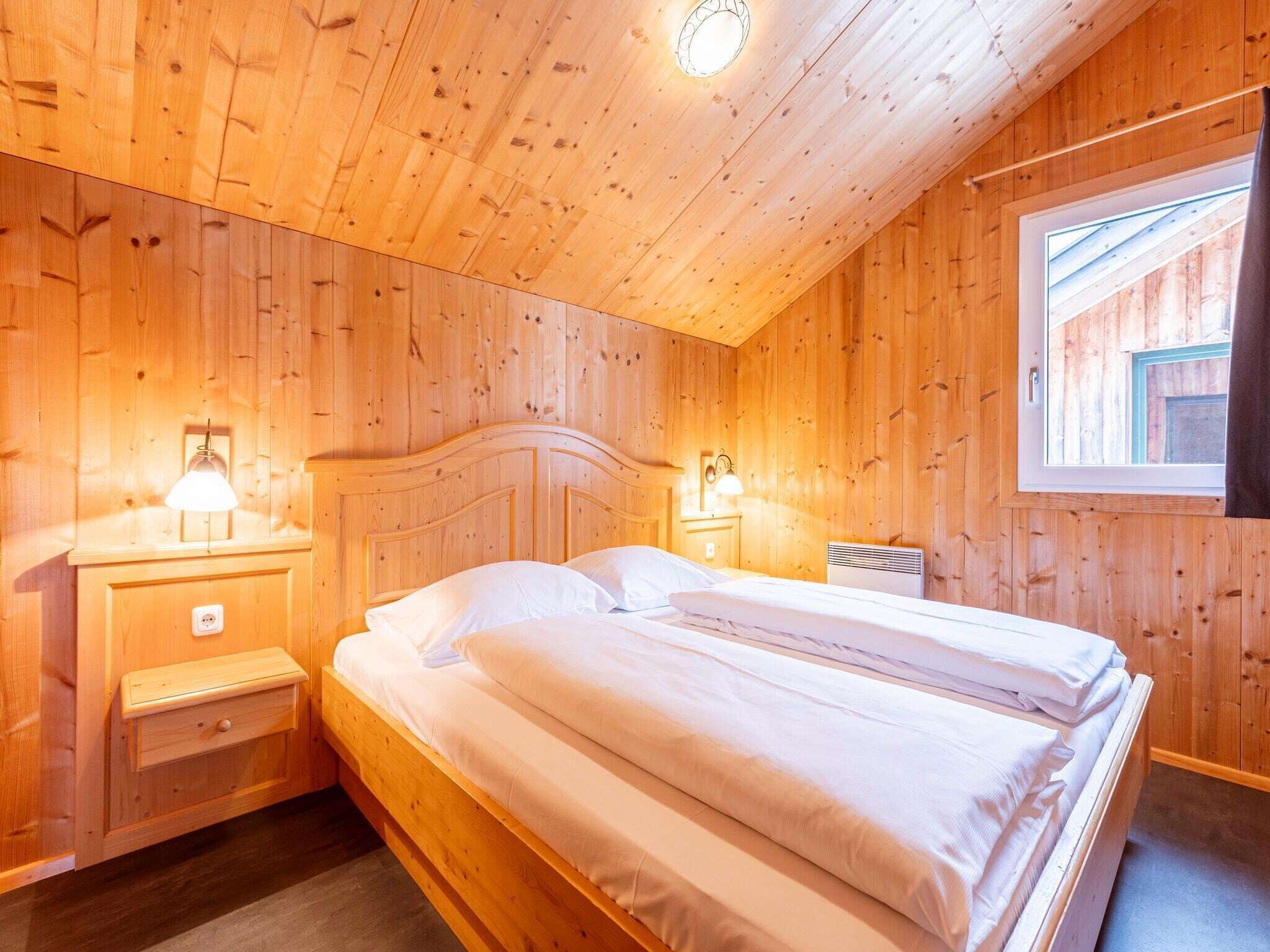 Une chambre à coucher aux murs lambrissés, avec un lit, des lampes de chevet et une fenêtre.